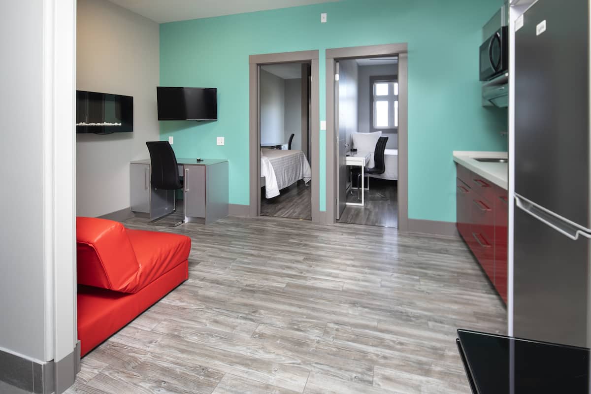 A modern hotel room with a red sofa, a desk, a bed, and a TV mounted on the wall.