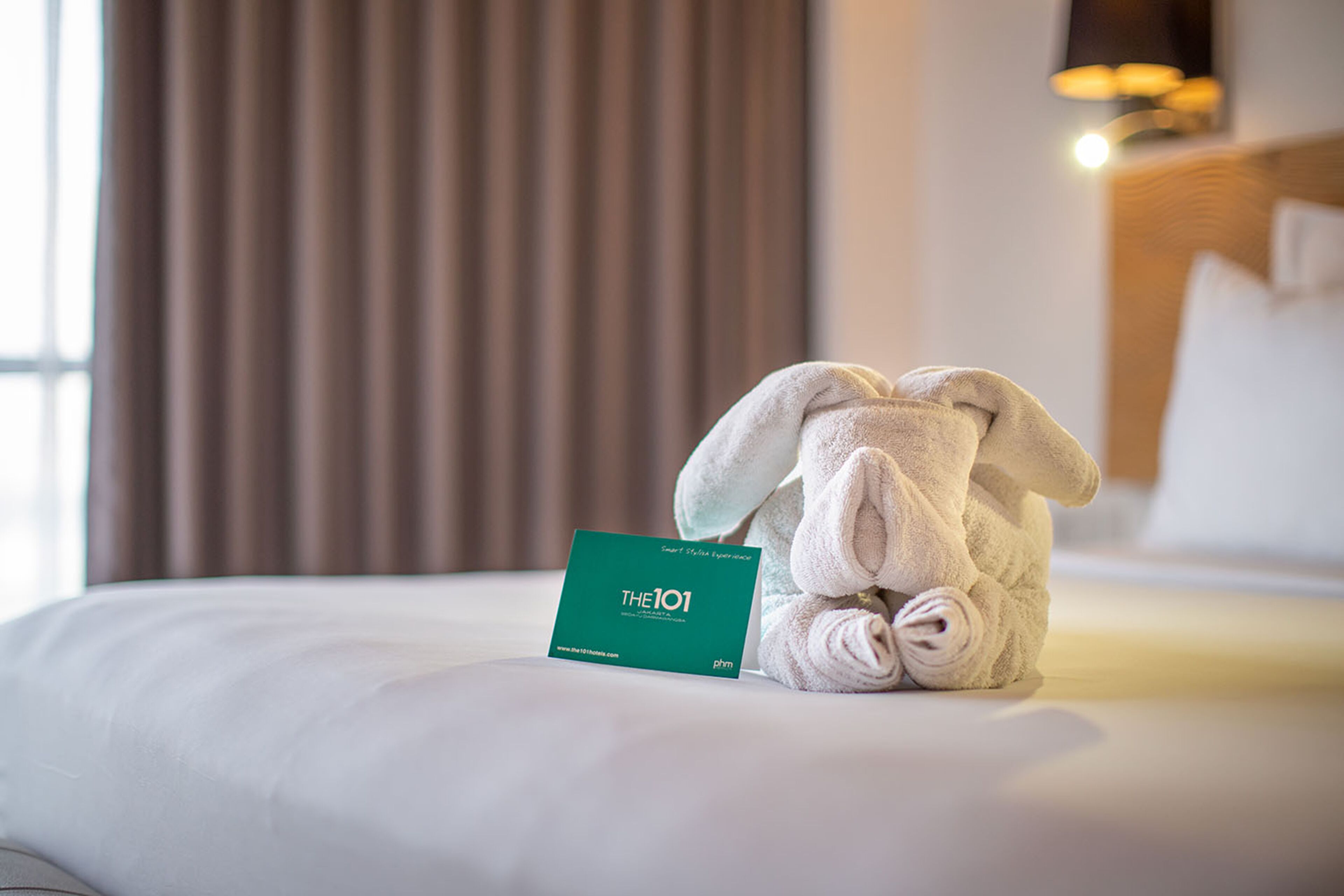 A neatly made bed with a folded towel and a business card on it.