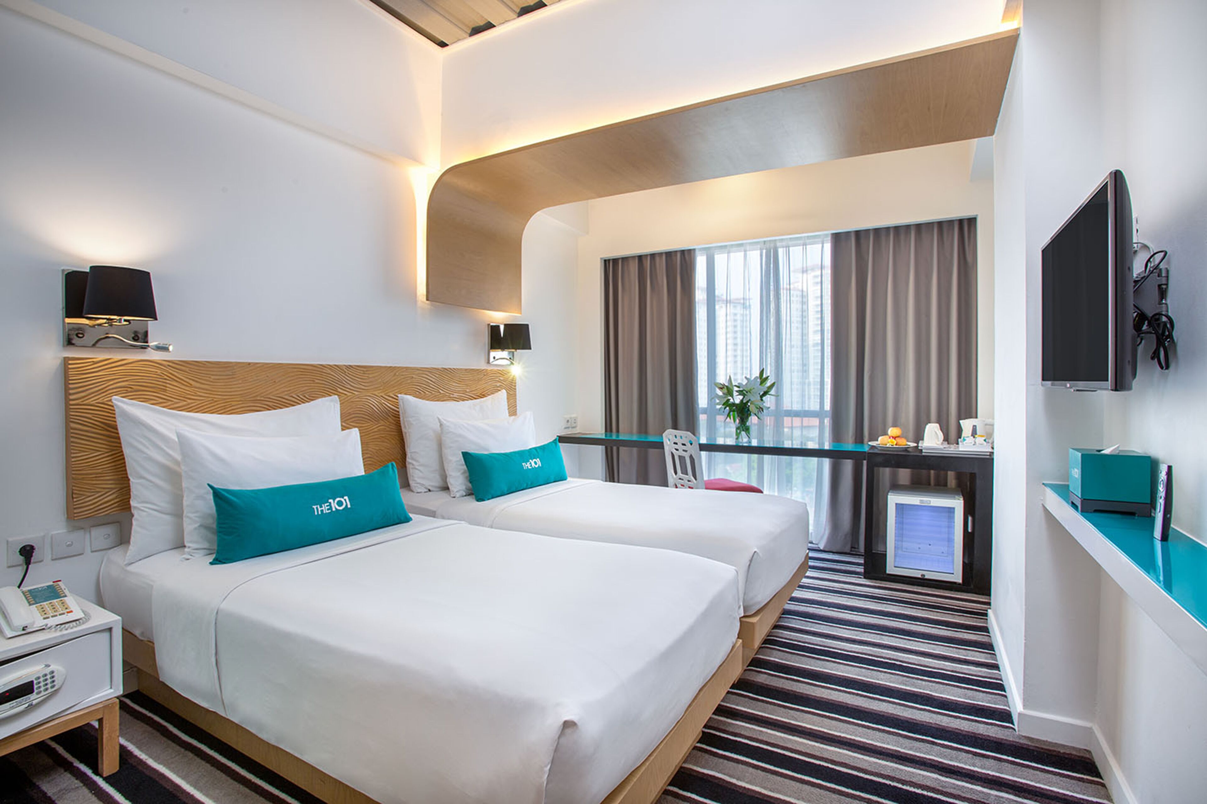 A hotel room with two beds, a desk with a computer, a TV, and a window with curtains.