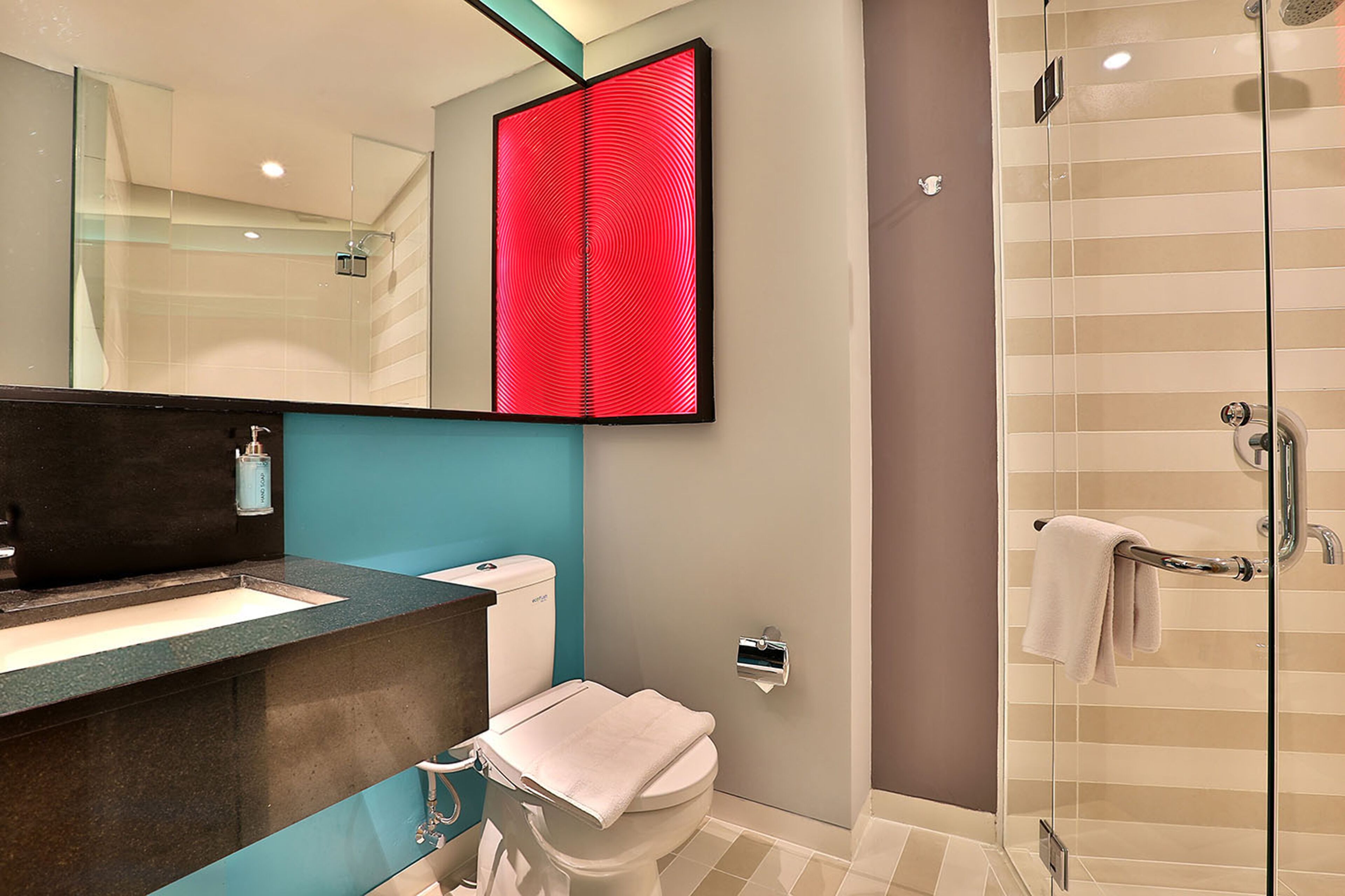 A modern bathroom with a glass shower enclosure, a white toilet, and a large mirror with a red abstract design.