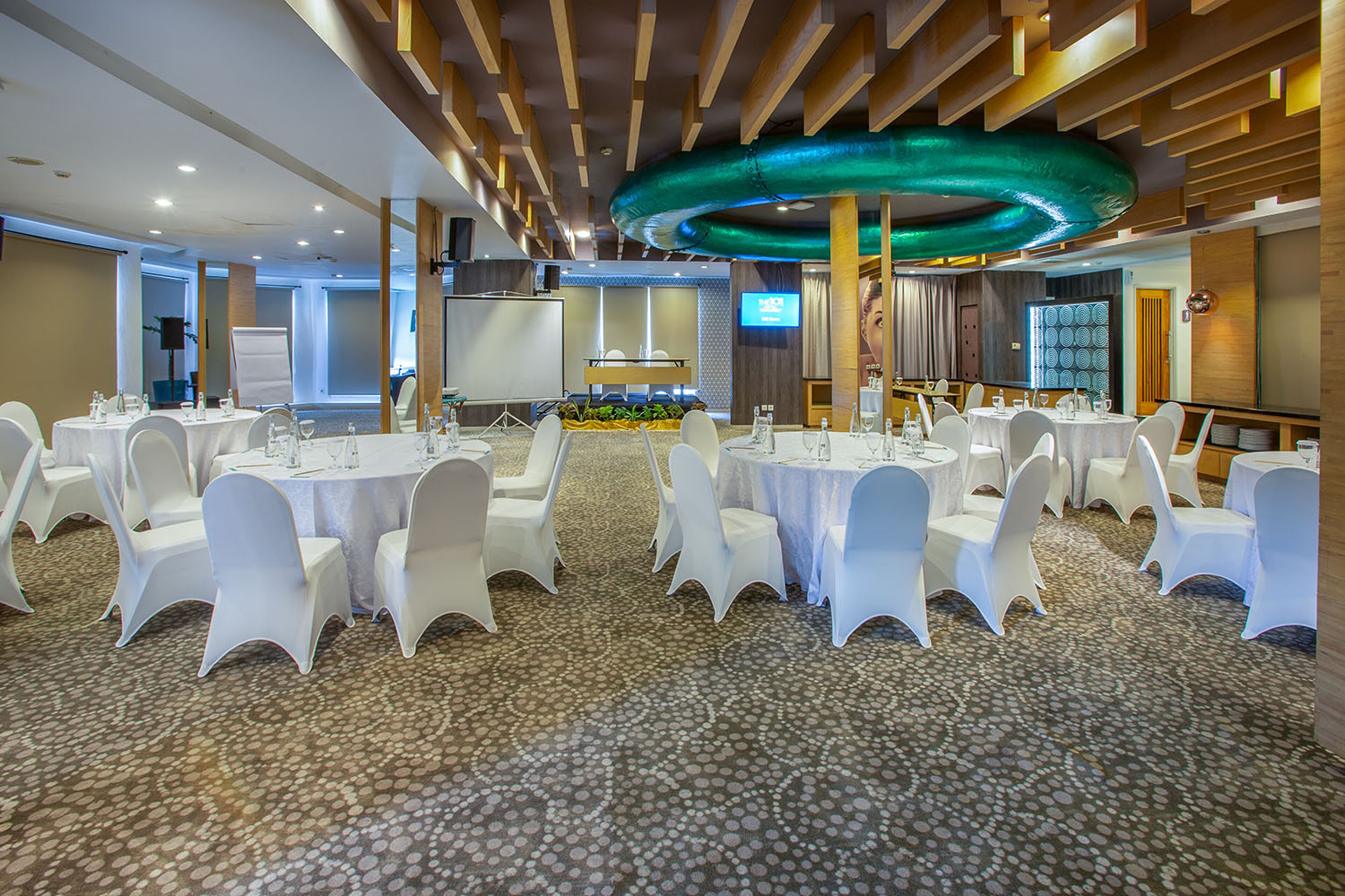 A conference room with round tables, white chairs, and a carpeted floor.