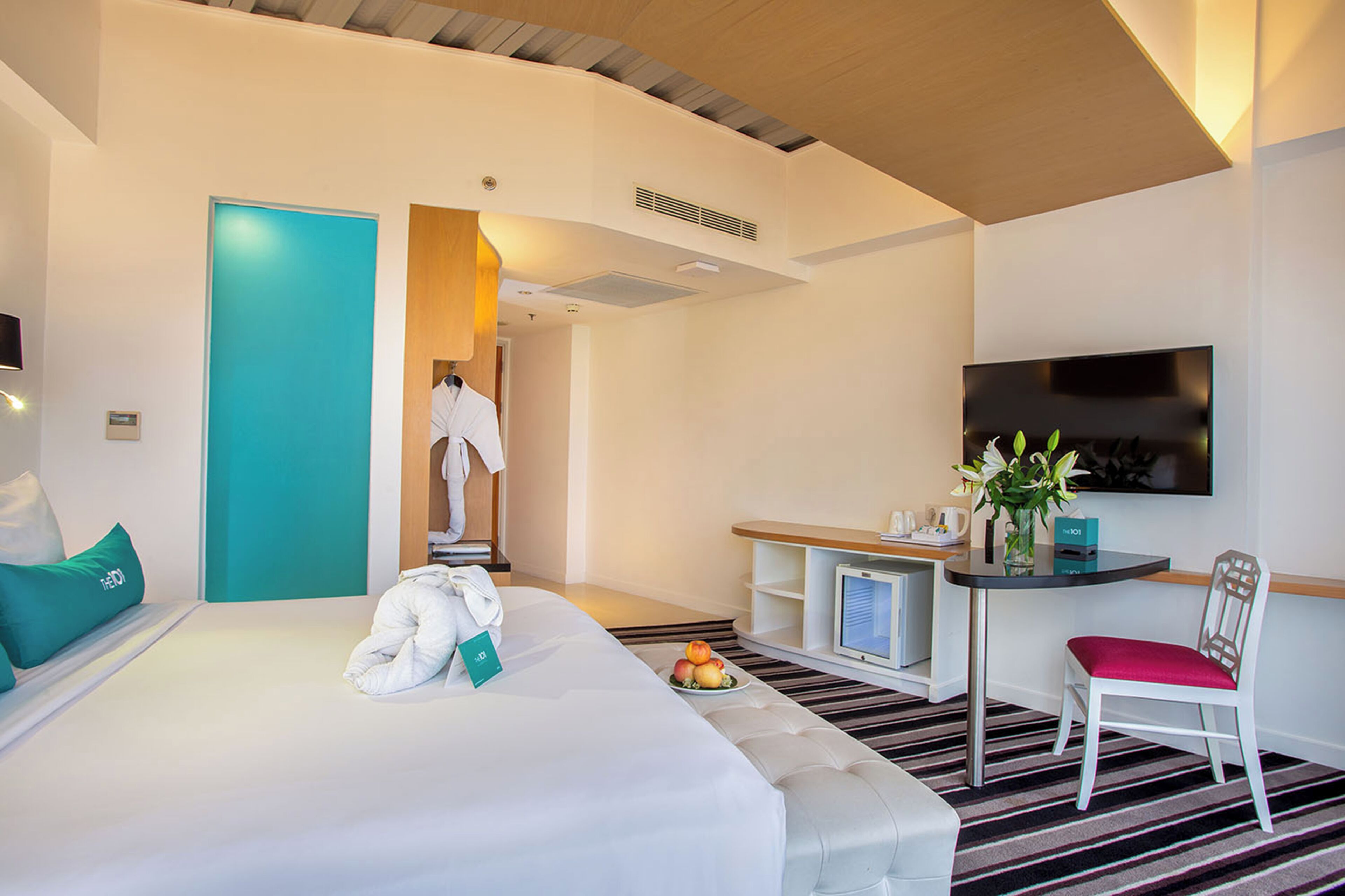 A hotel room with a bed, a desk with a chair, a TV, and a bathroom visible through an open door.