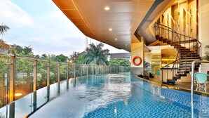 Une piscine intérieure à débordement avec une paroi en verre, un espace bar et un escalier menant à un niveau supérieur.