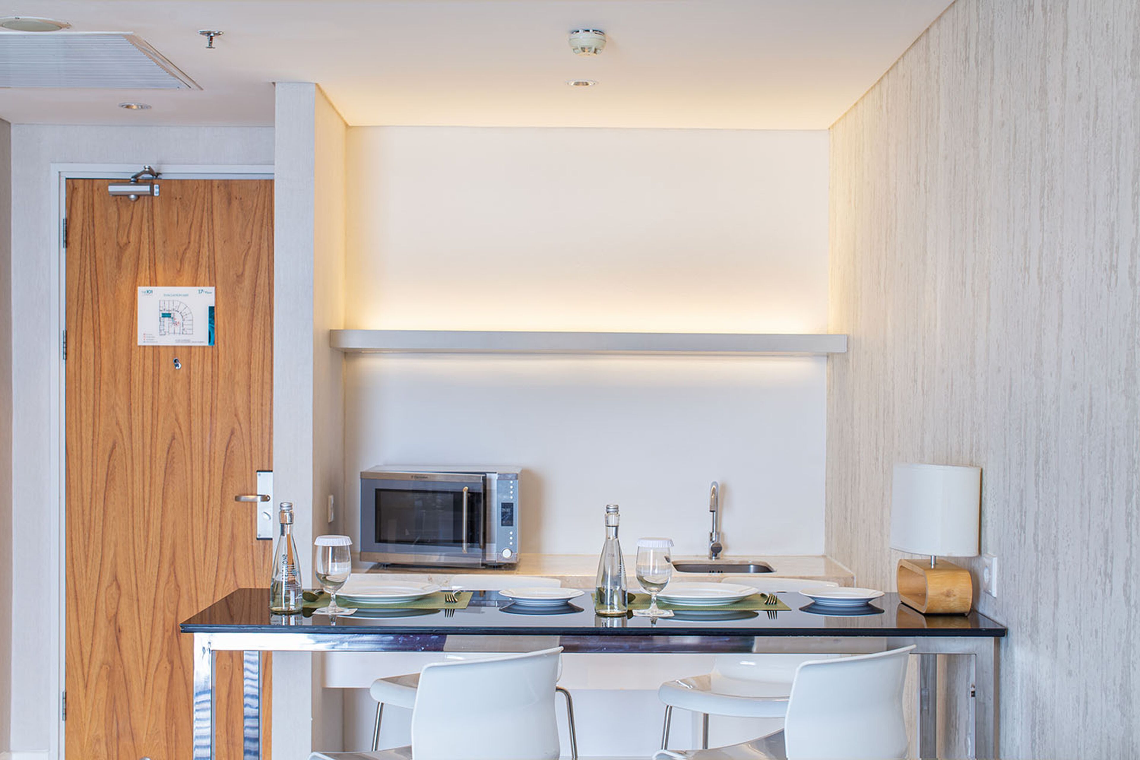 A modern kitchen with a microwave, a sink, and a dining area with white chairs and a glass table.