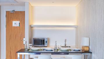 A modern kitchen with a microwave, a sink, and a dining area with white chairs and a glass table.