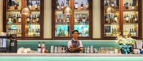 A bar area with wooden cabinets displaying bottles, a bar counter with stools, and a hanging light fixture.