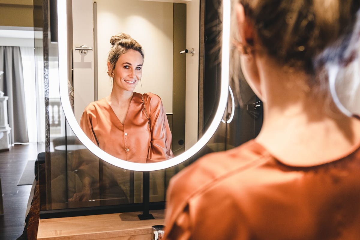 A bathroom with a round mirror, wooden vanity, and a sink.