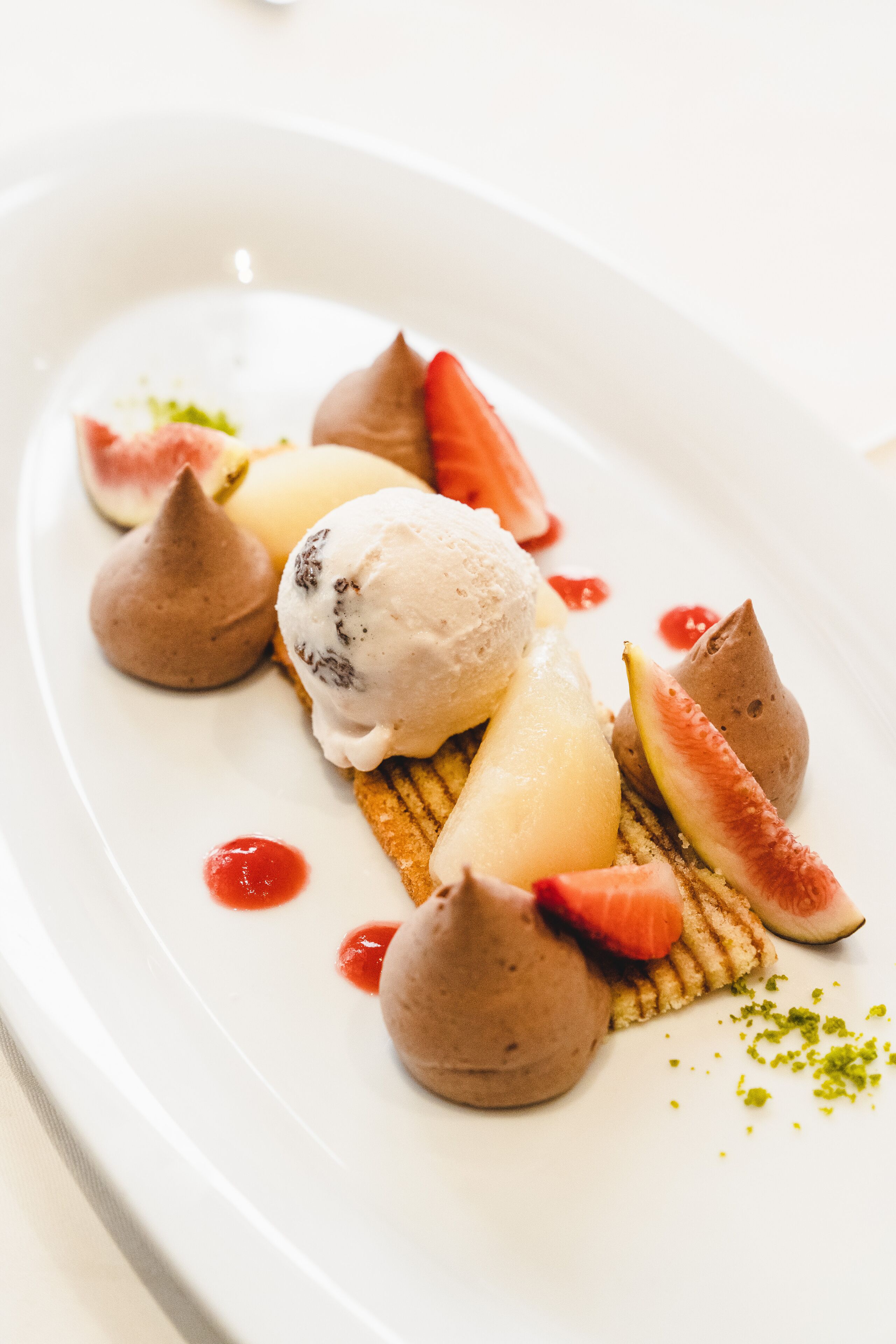 A dessert plate with ice cream, fruit, and chocolate shapes.