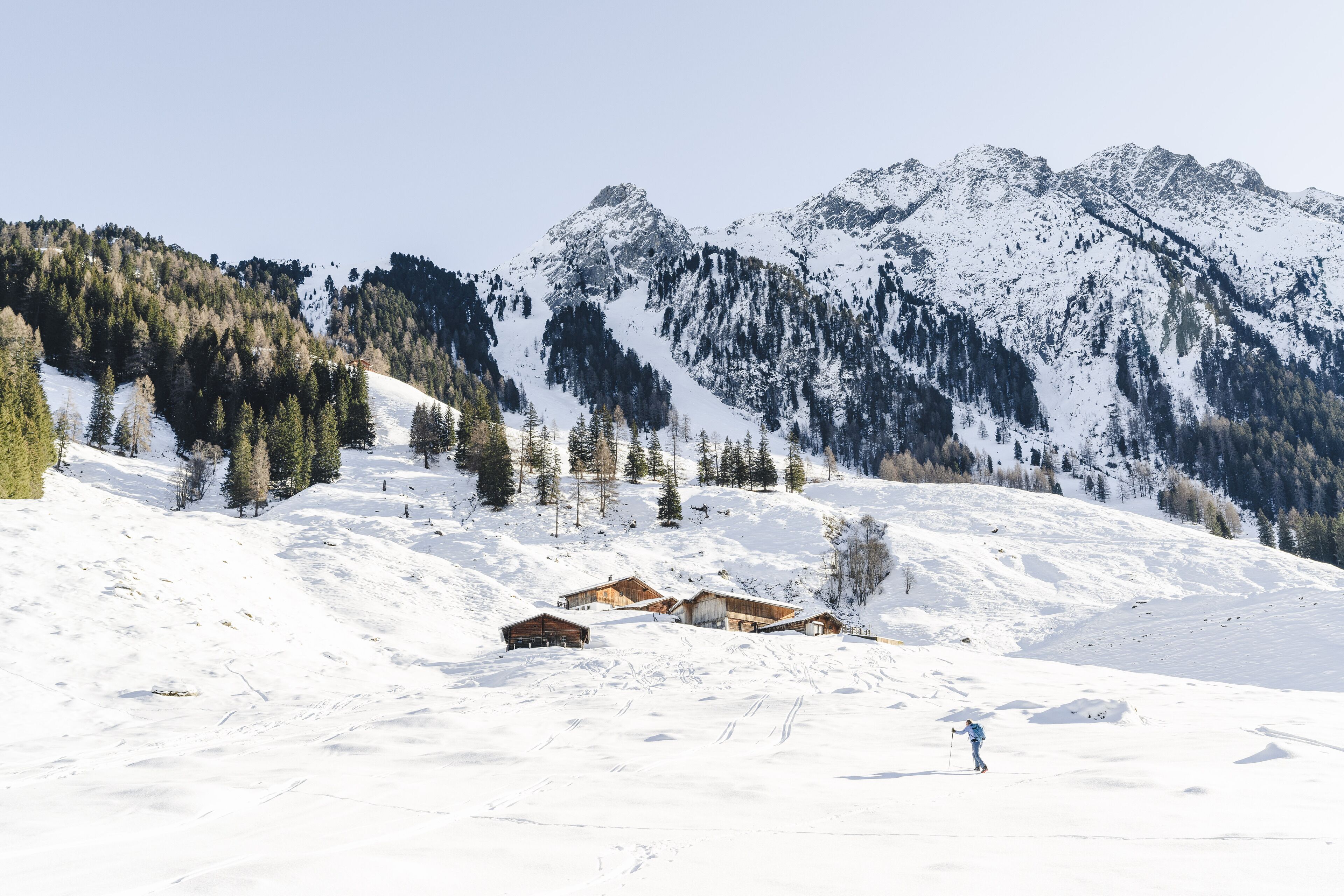 A snow-covered mountain landscape with wooden cabins and a skier.