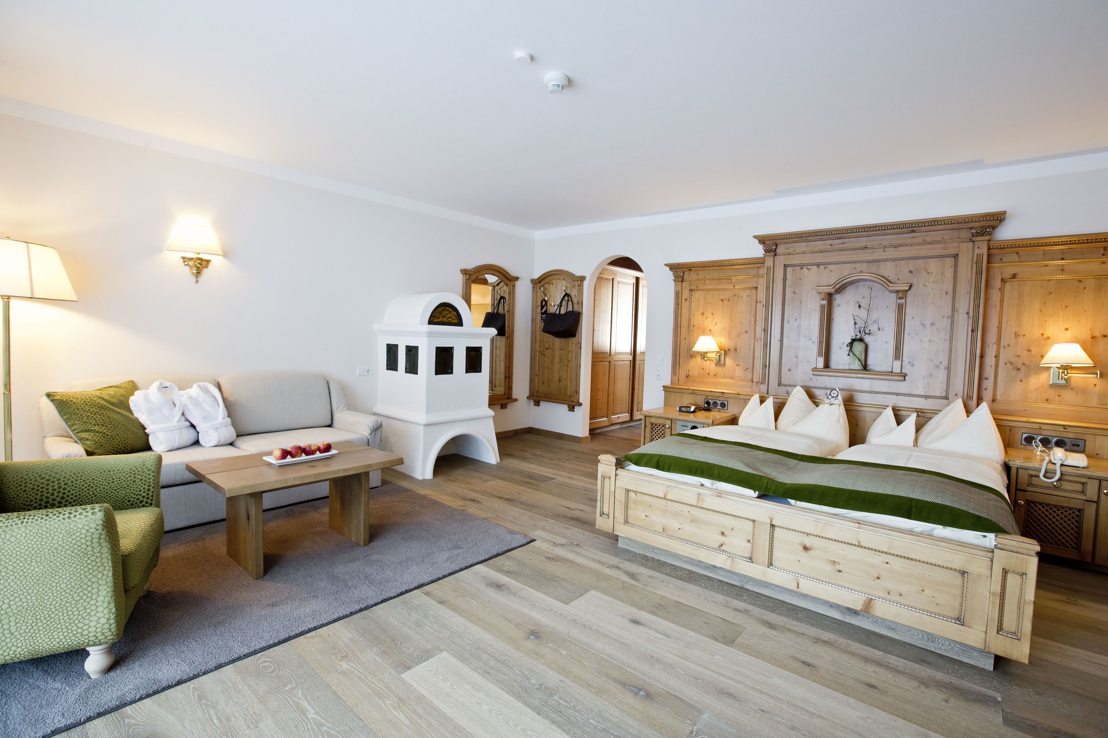 A room with a bed, a sofa, a small table, and a chair. There are wall sconces and a mirror.
