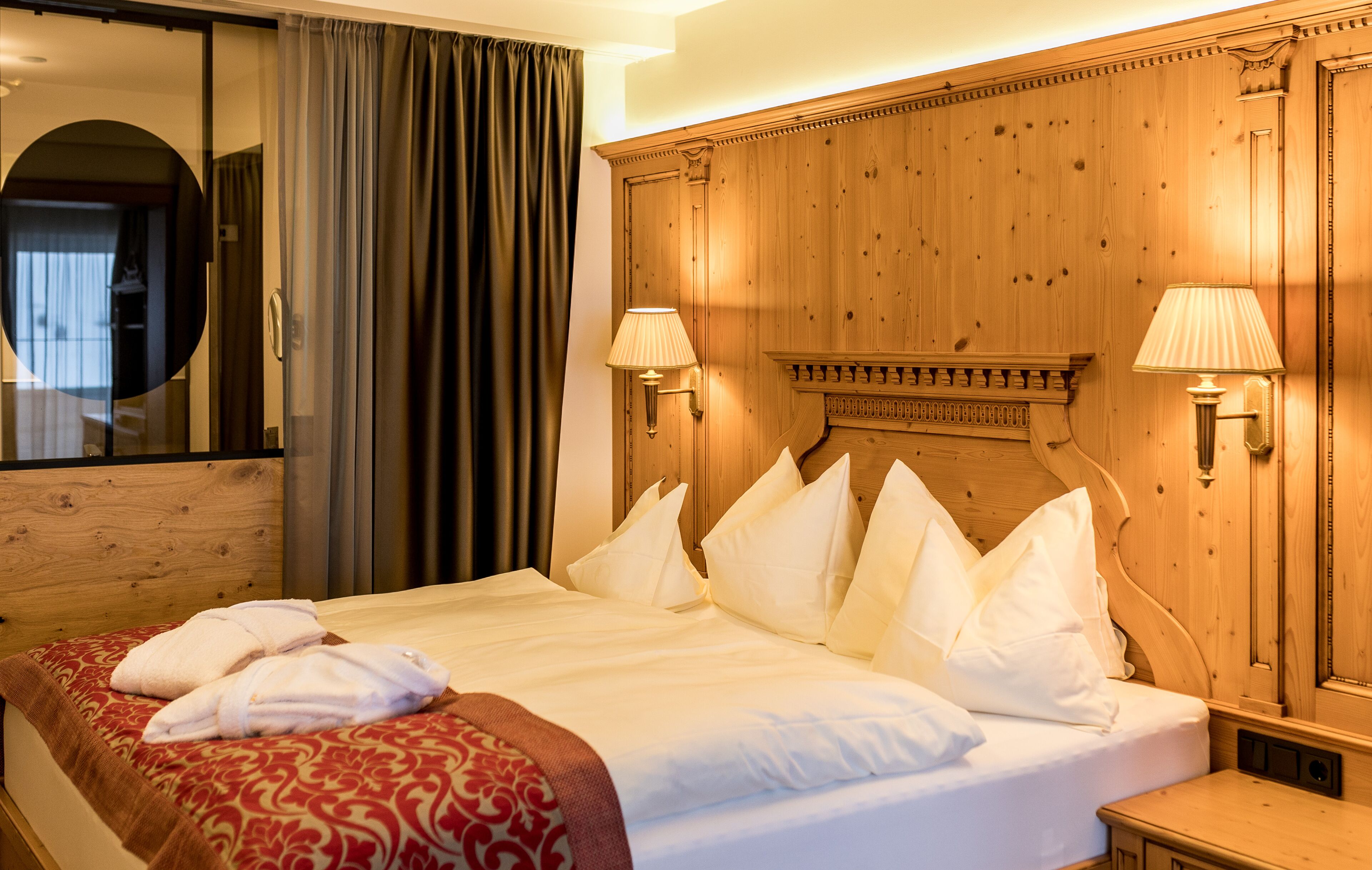 A hotel room with a large bed, two bedside lamps, a wooden headboard, and a mirror.