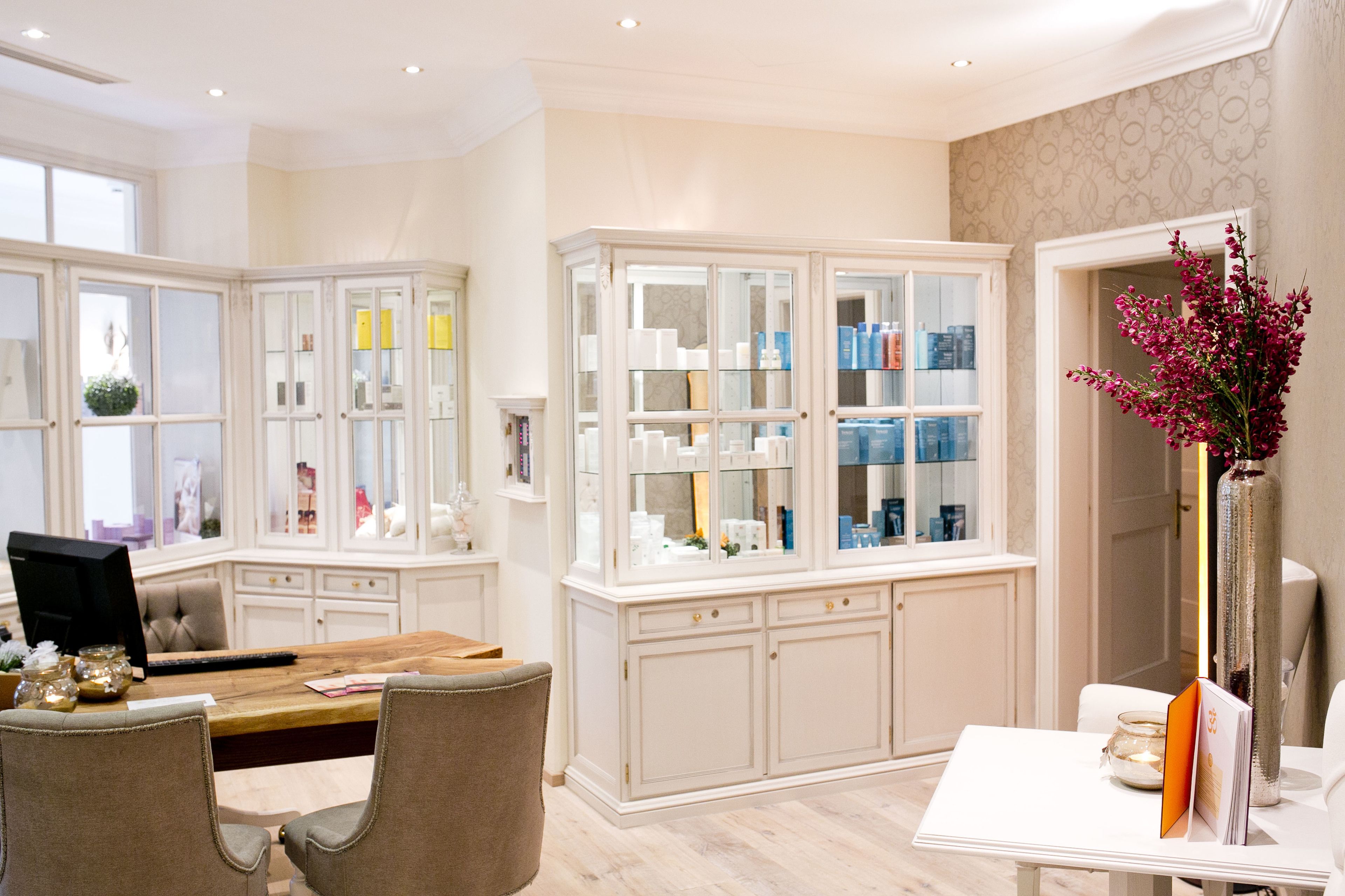 Una habitación luminosa con una mesa de comedor de madera, sillas color beige y un armario blanco con puertas de cristal que exhibe varios objetos.