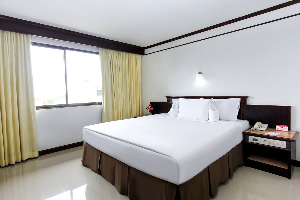 A hotel room with a large bed, a bedside table with a phone and a lamp, and a window with curtains.