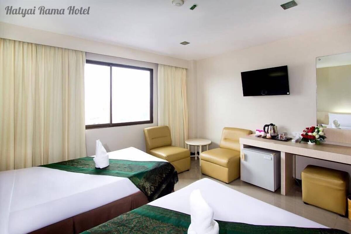 A hotel room with two beds, a desk, a chair, a small table, a TV, and a minibar.