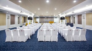 A conference room with rows of white tables and chairs, a stage with a podium, and a large screen. - Hat Yai Rama Hotel (Hat Yai)