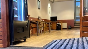 Un vestíbulo de hotel con mostrador de recepción, sillas, televisor y máquina expendedora.