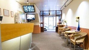 Zona de recepción de hotel con un mostrador de madera, un televisor montado en la pared y varias sillas de mimbre dispuestas para los huéspedes.