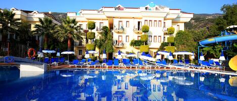 A hotel with a swimming pool, blue lounge chairs, and umbrellas.