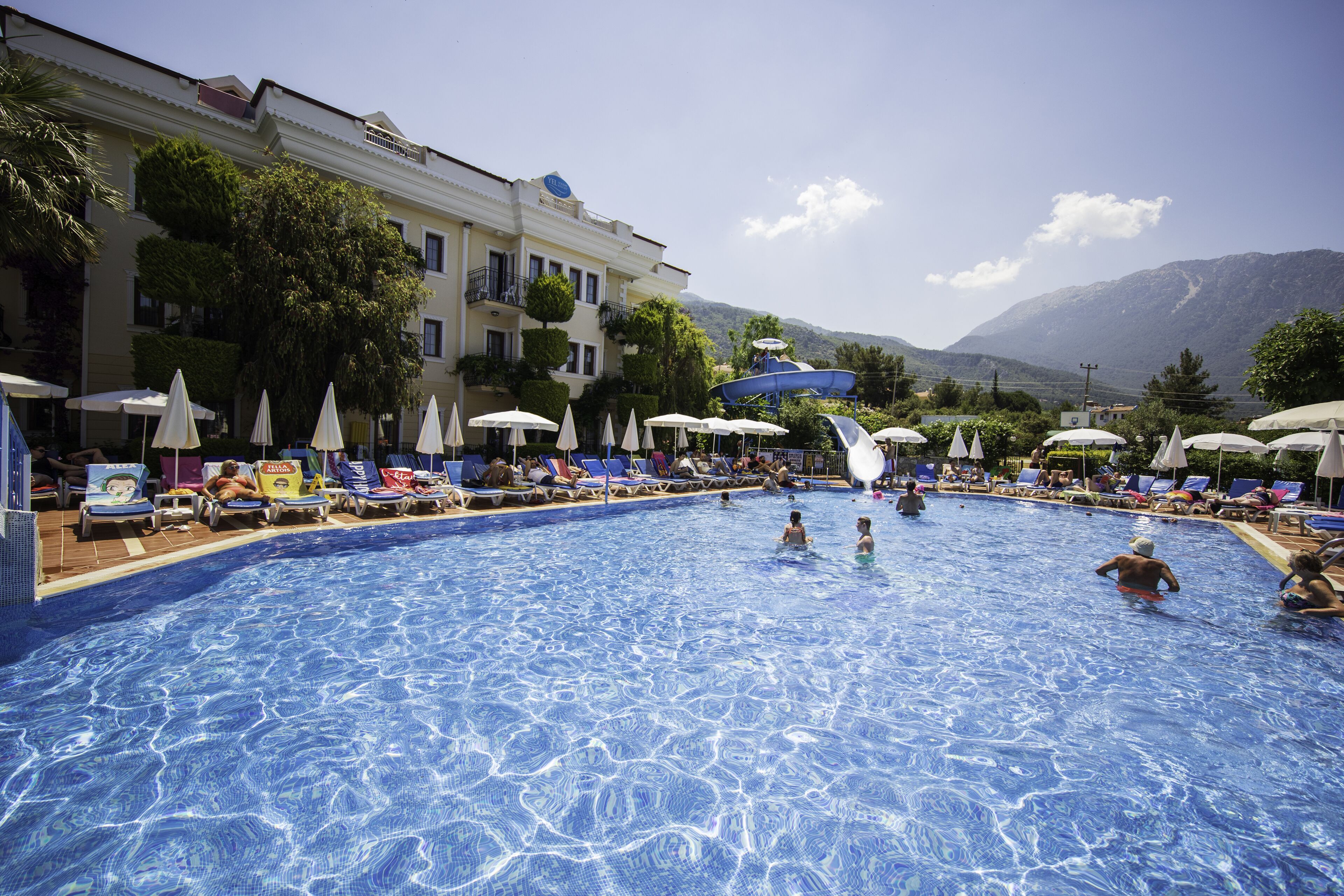 A swimming pool with lounge chairs and umbrellas, surrounded by a building with a mountain view.