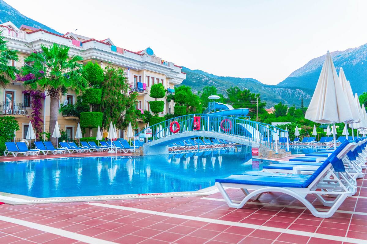A swimming pool with blue lounge chairs, a bridge, and a mountain backdrop.