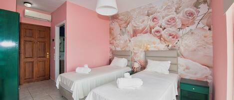 A hotel room with two beds, a floral wall mural, a wooden door, and a green nightstand.