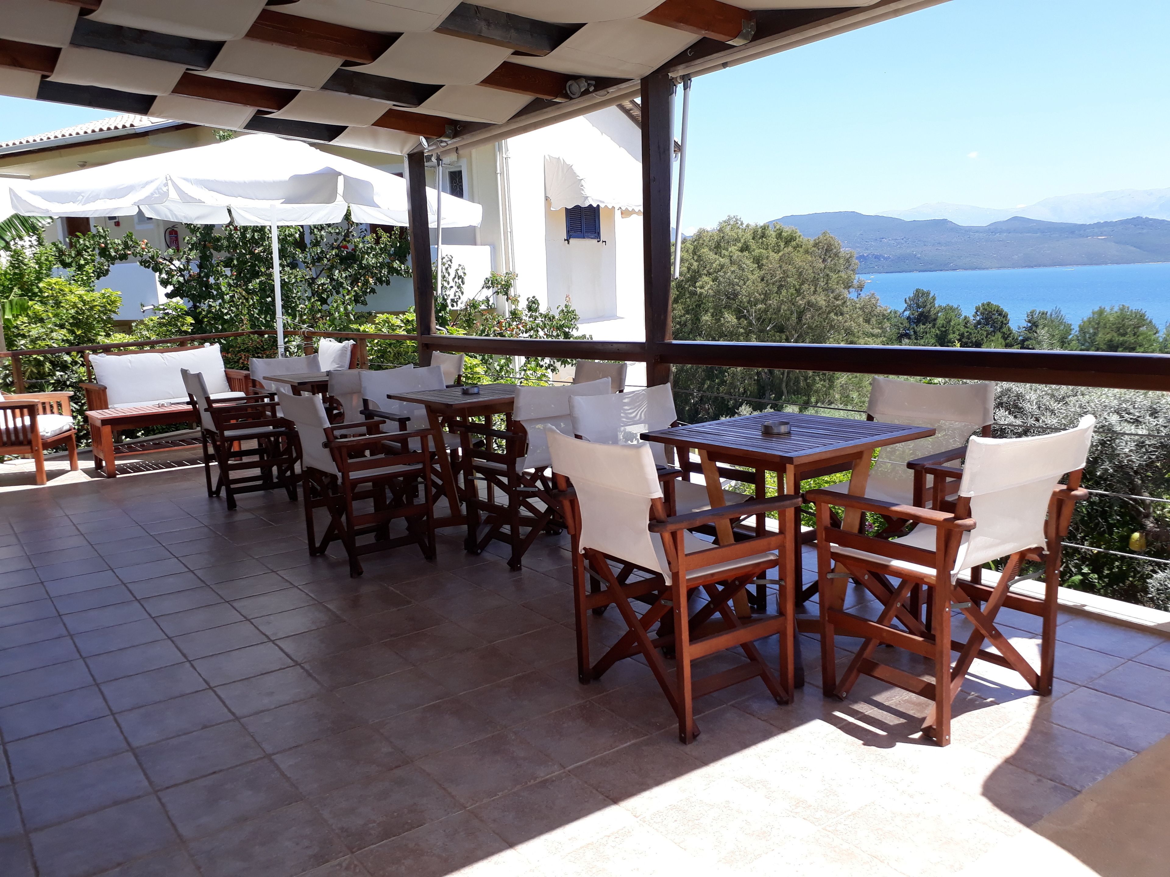 An outdoor patio with wooden furniture and white cushions, overlooking a scenic view of mountains and a body of water.