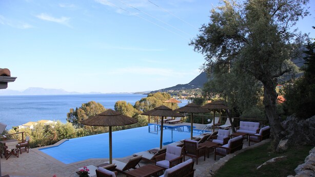 Área de piscina com espreguiçadeiras e guarda-sóis, com vista para um corpo d'água e uma paisagem montanhosa.