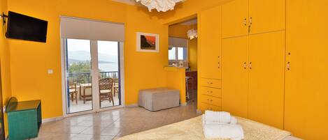 A bright yellow room with a bed, a TV, and a balcony with a view.