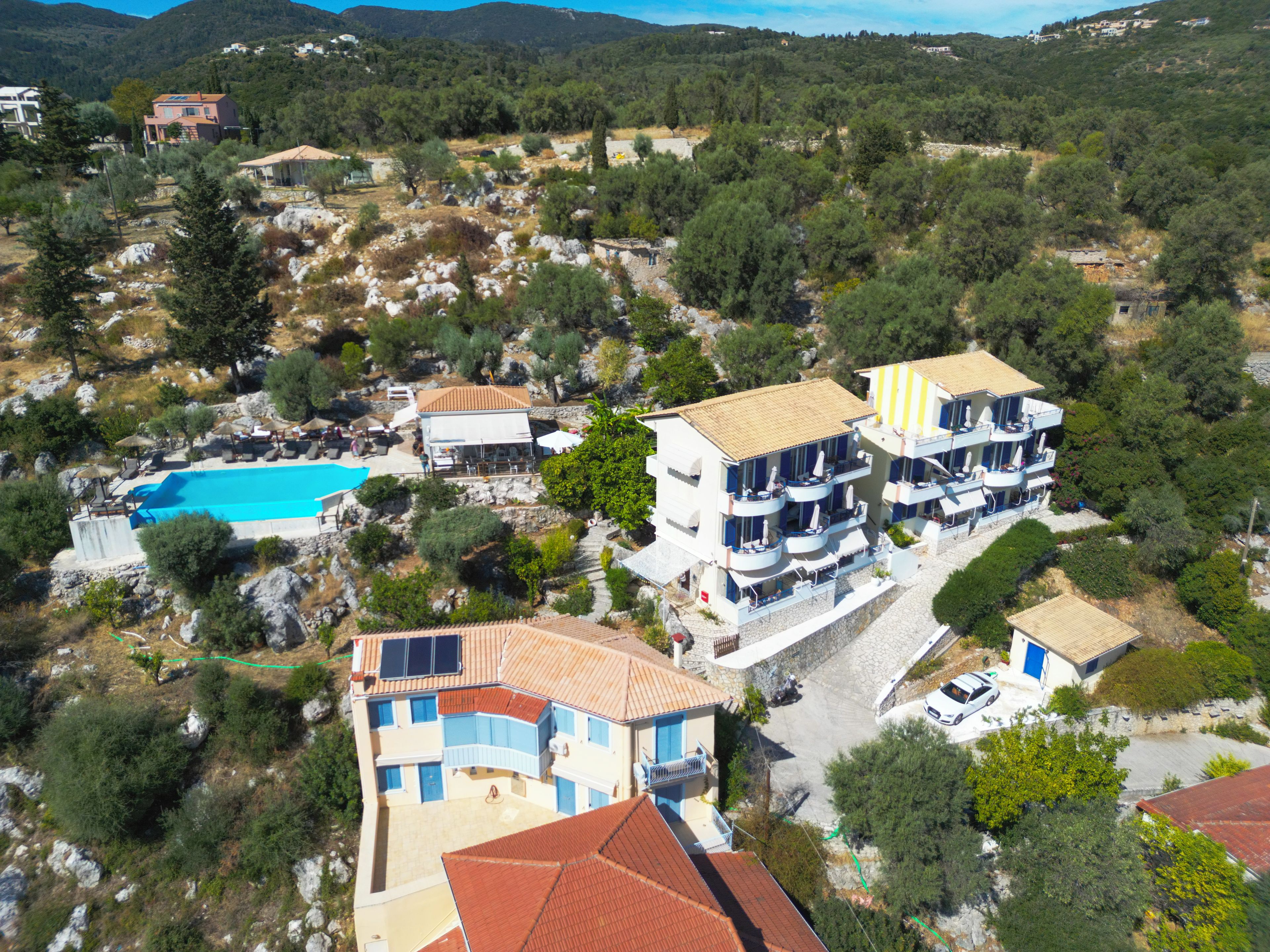 A residential area with multiple buildings, a swimming pool, and a mountainous backdrop.