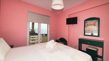 A pink-themed hotel room with a bed, a desk, a chair, a TV, and a window with a view.