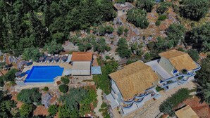 Vista aérea de um resort com piscina, espreguiçadeiras e vários edifícios com telhados de cerâmica.