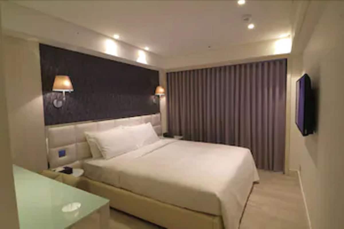 Quarto de hotel com cama, abajures, televisão e janela com cortinas.