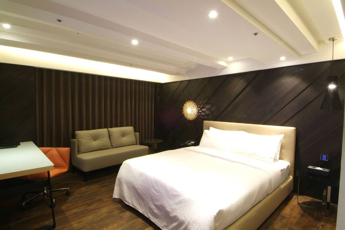 Quarto de hotel moderno com uma cama grande, um sofá, uma escrivaninha e uma mesinha.