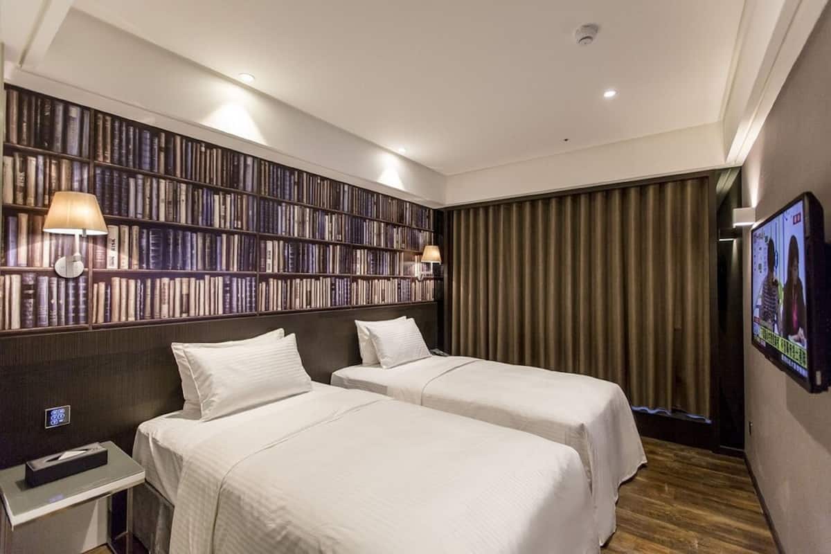 Quarto de hotel com duas camas, uma estante de livros, uma televisão e uma mesa de cabeceira.
