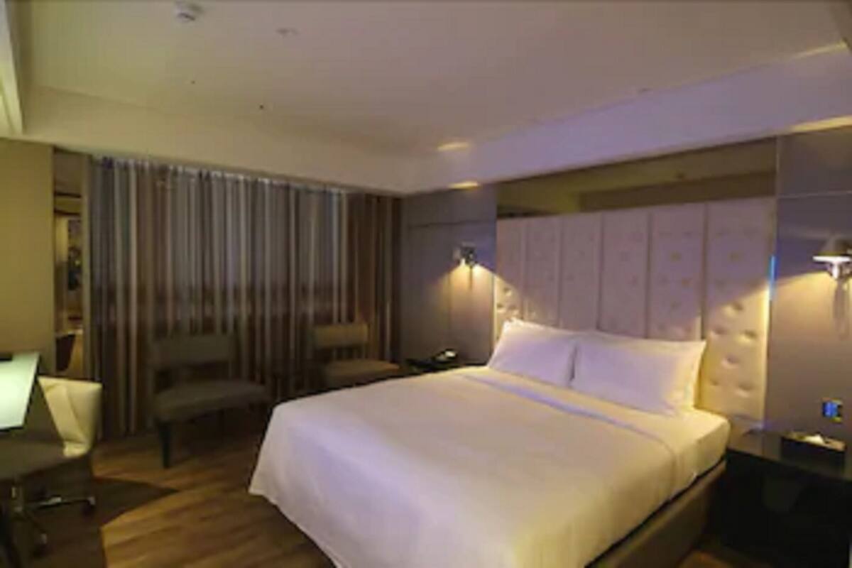 Quarto de hotel com cama grande, escrivaninha, cadeira e mesa de cabeceira com abajur.