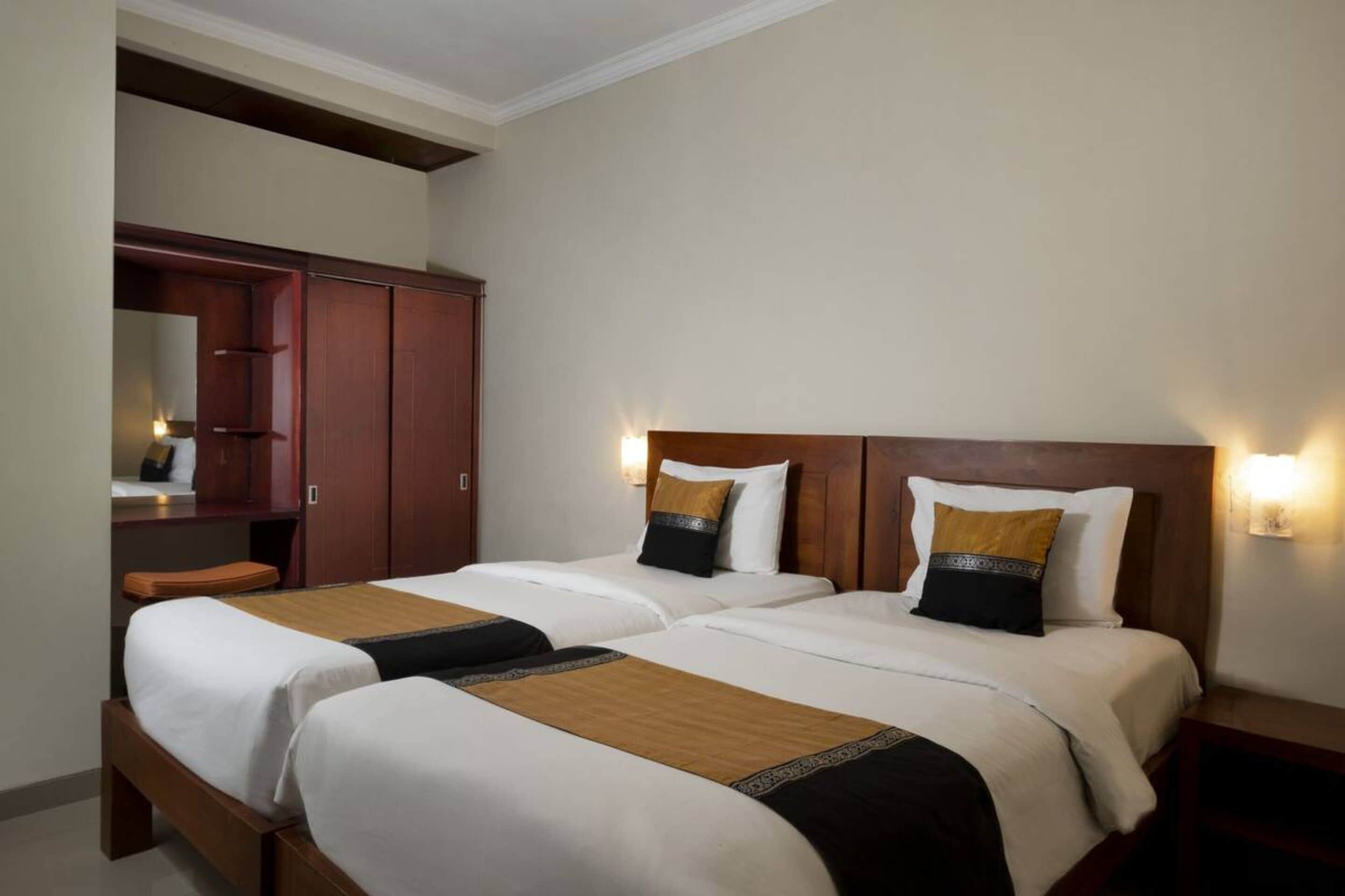 A hotel room with two beds, a wardrobe, and a nightstand.