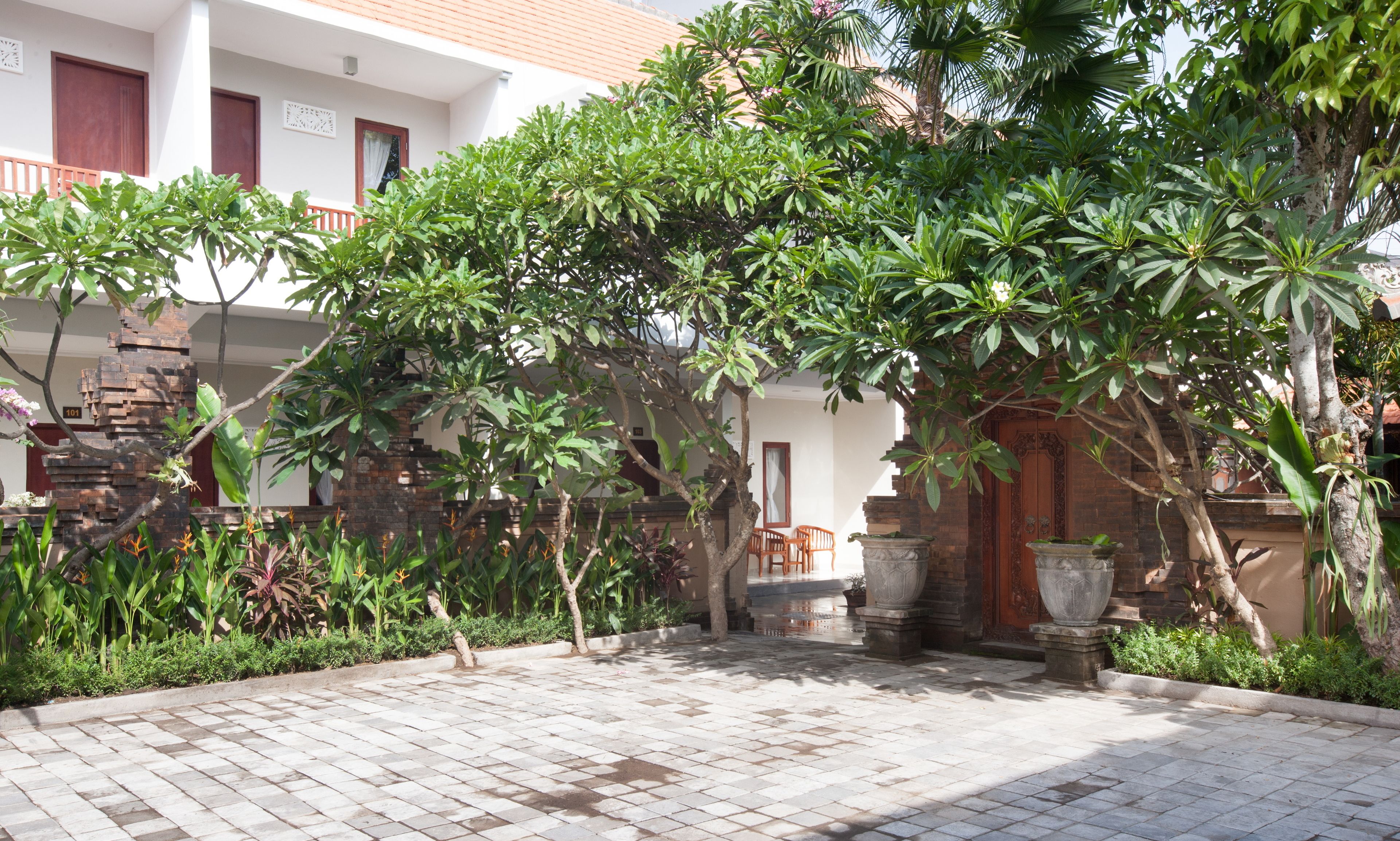 Un patio con suelo de baldosas, rodeado de abundante follaje y un muro de piedra.