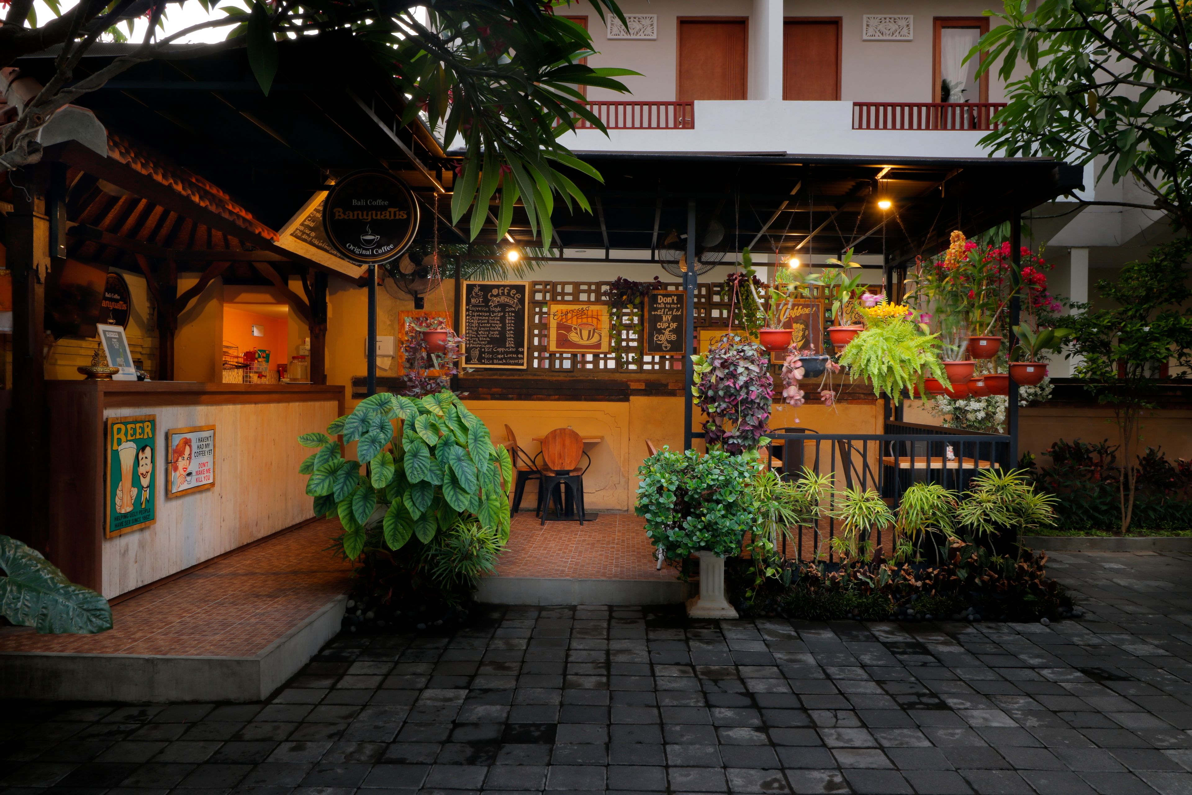 A cozy outdoor seating area with a coffee shop, wooden tables, and potted plants.