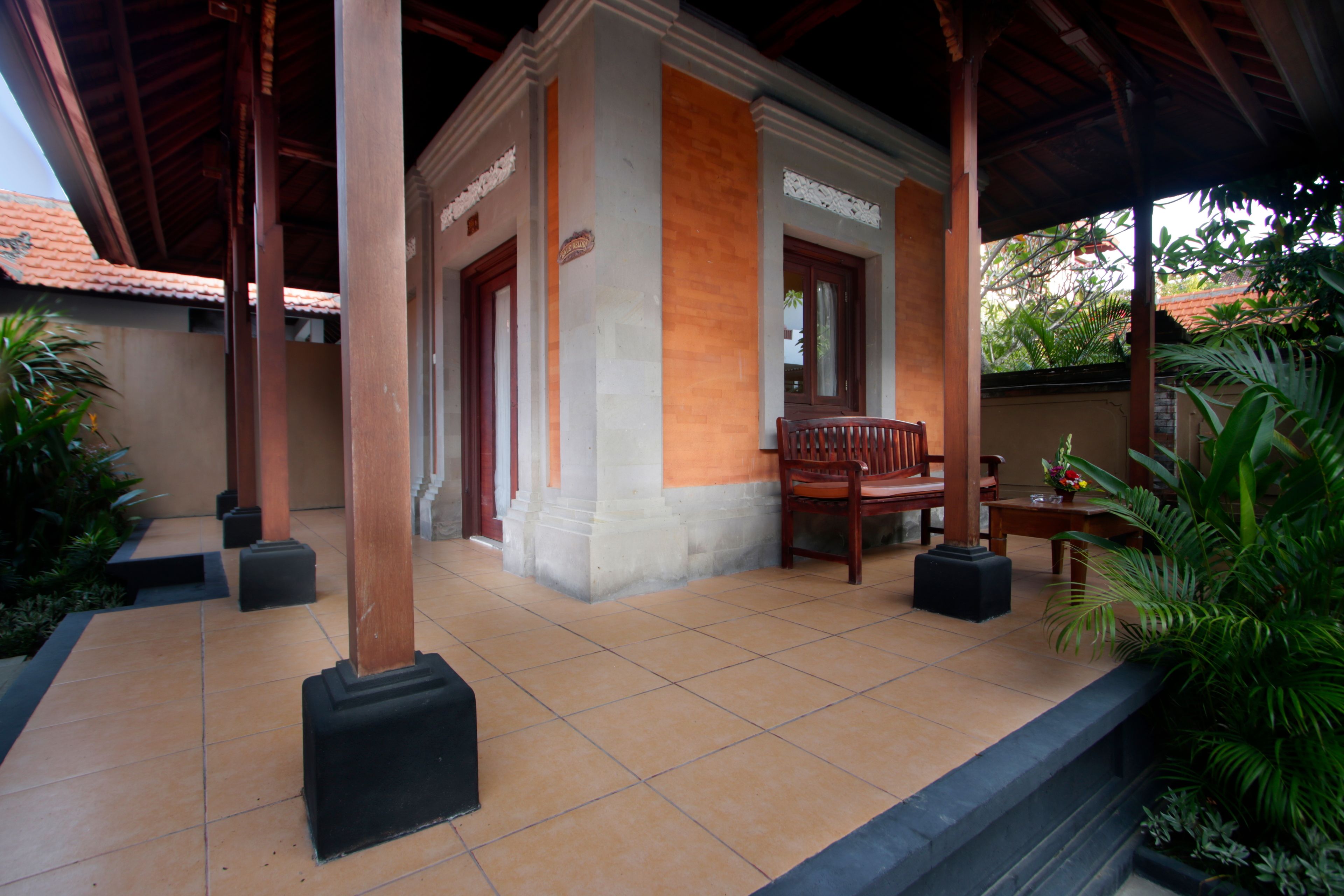 A covered outdoor area with a tiled floor, wooden columns, and a bench.