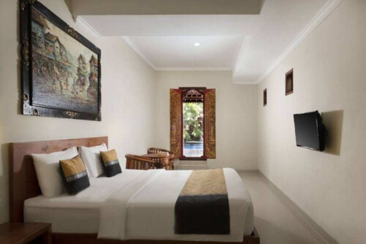 A hotel room with a bed, a television, a painting, and a window with curtains.