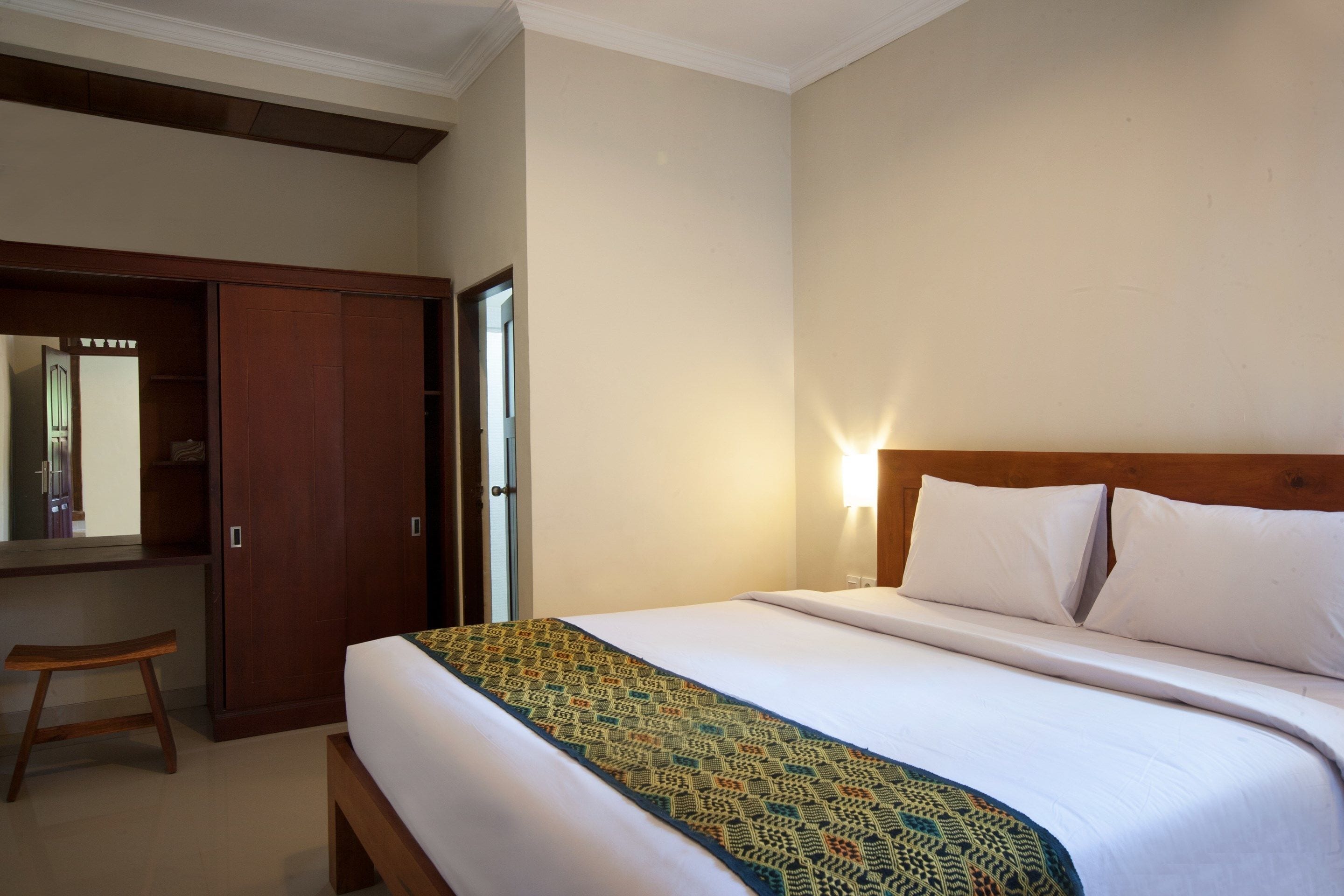 Una habitación de hotel con una cama, un banco de madera, un armario y un espejo.