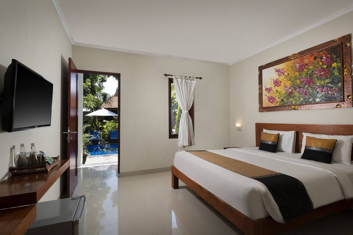 A hotel room with a bed, a TV, a desk, and a window with curtains.
