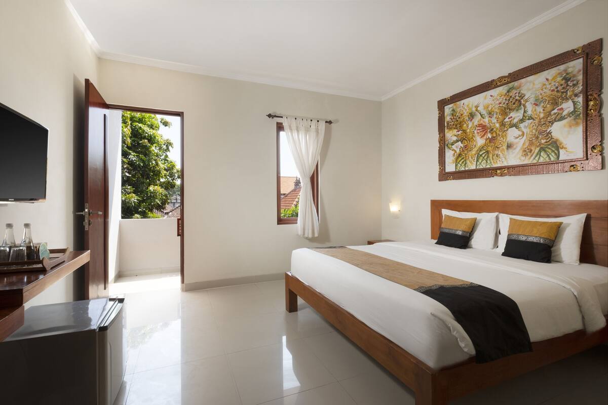 A hotel room with a bed, a television, a window with curtains, and a painting on the wall.