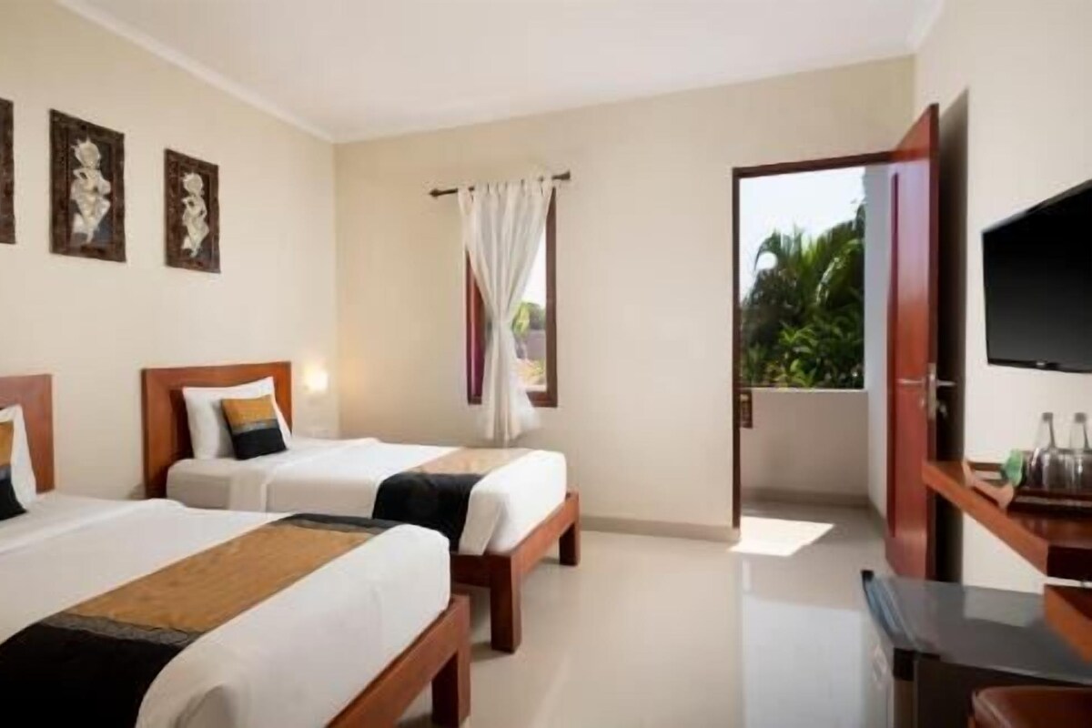 A hotel room with two beds, a TV, and a balcony with a view of greenery.