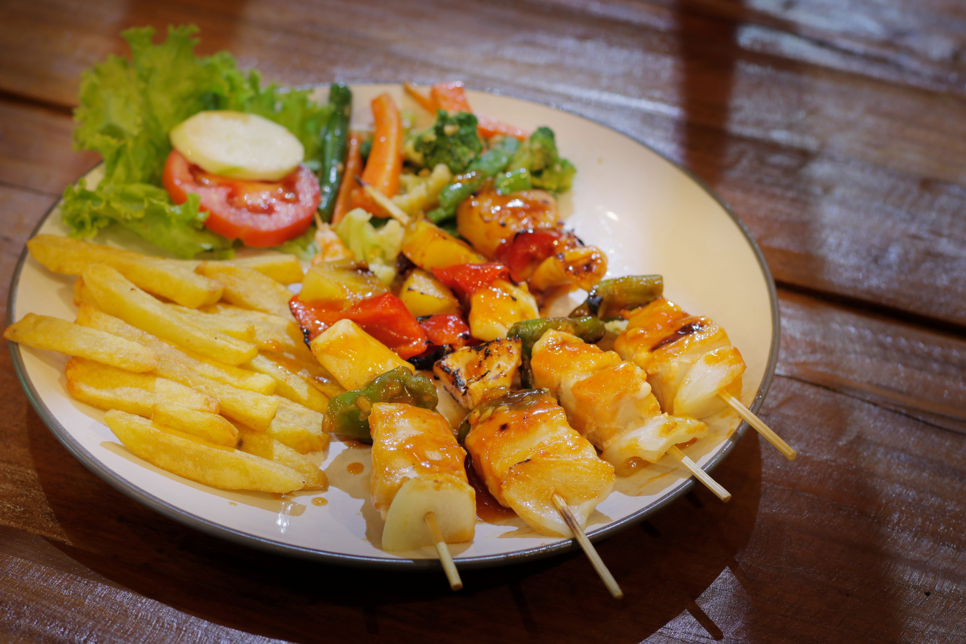 A plate of food with grilled vegetables, chicken skewers, and French fries.