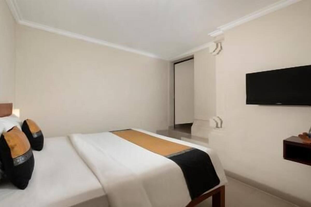 A hotel room with a bed, a television mounted on the wall, and a small table with a bottle.