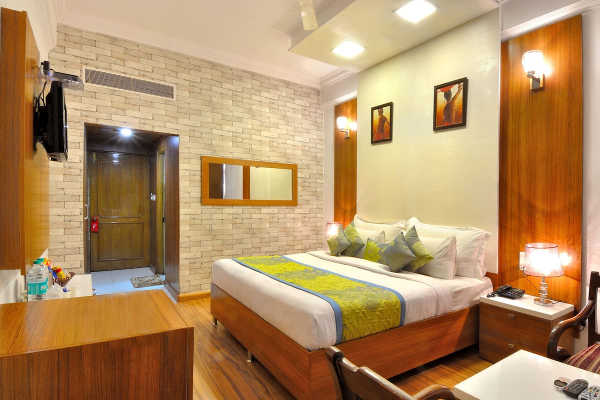 A hotel room with a brick wall, a wooden bed, a bedside table with a lamp, and a bathroom with a sink and mirror.