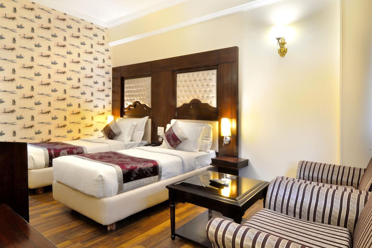 A hotel room with two beds, a sofa, a small table, and a wall with a ship pattern.