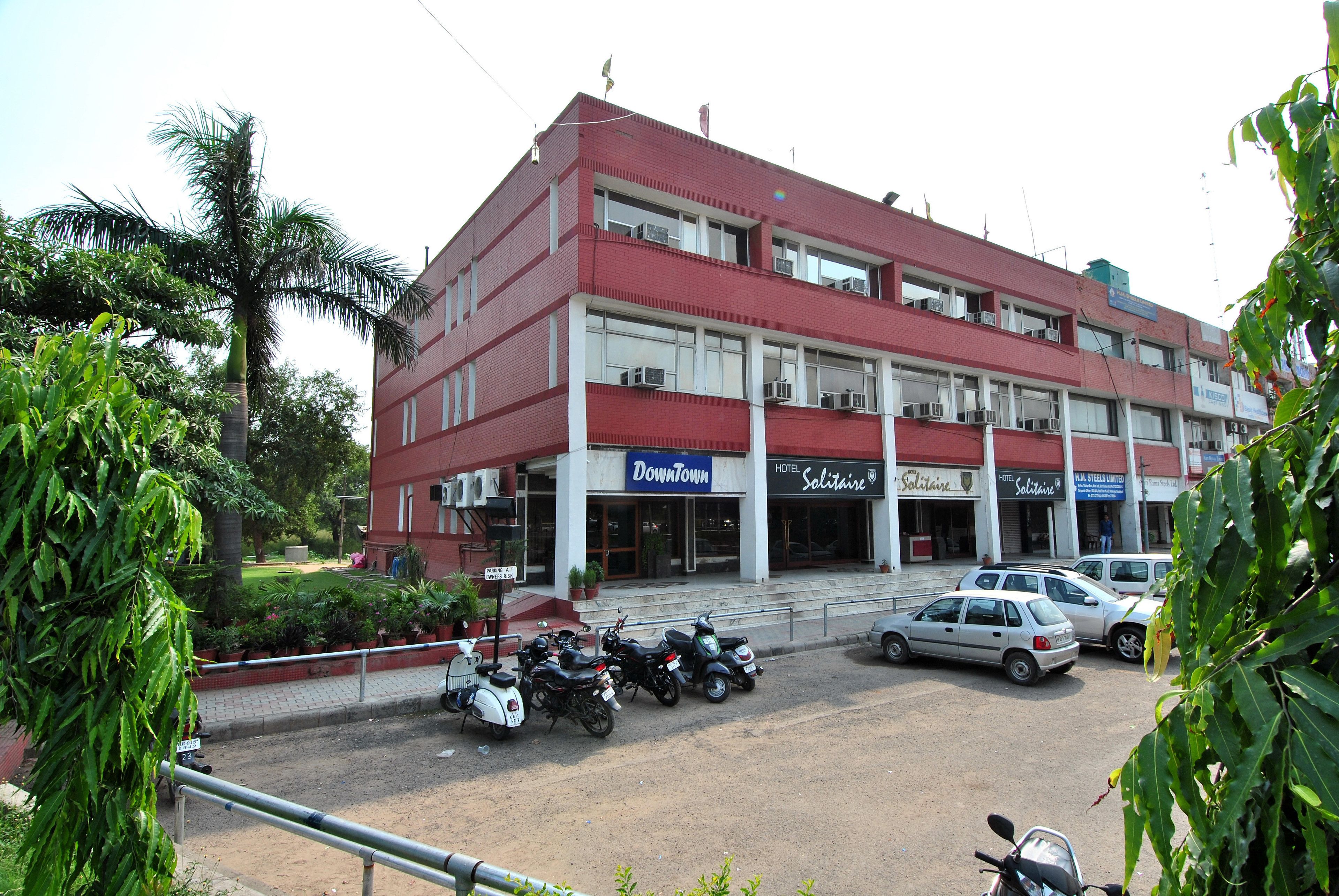 Um edifício de vários andares com fachada vermelha, apresentando uma placa com a inscrição 'Downtown', um hotel 'Solitaire' e uma placa 'PARK STRENGTH'. Várias motocicletas estão estacionadas na frente.