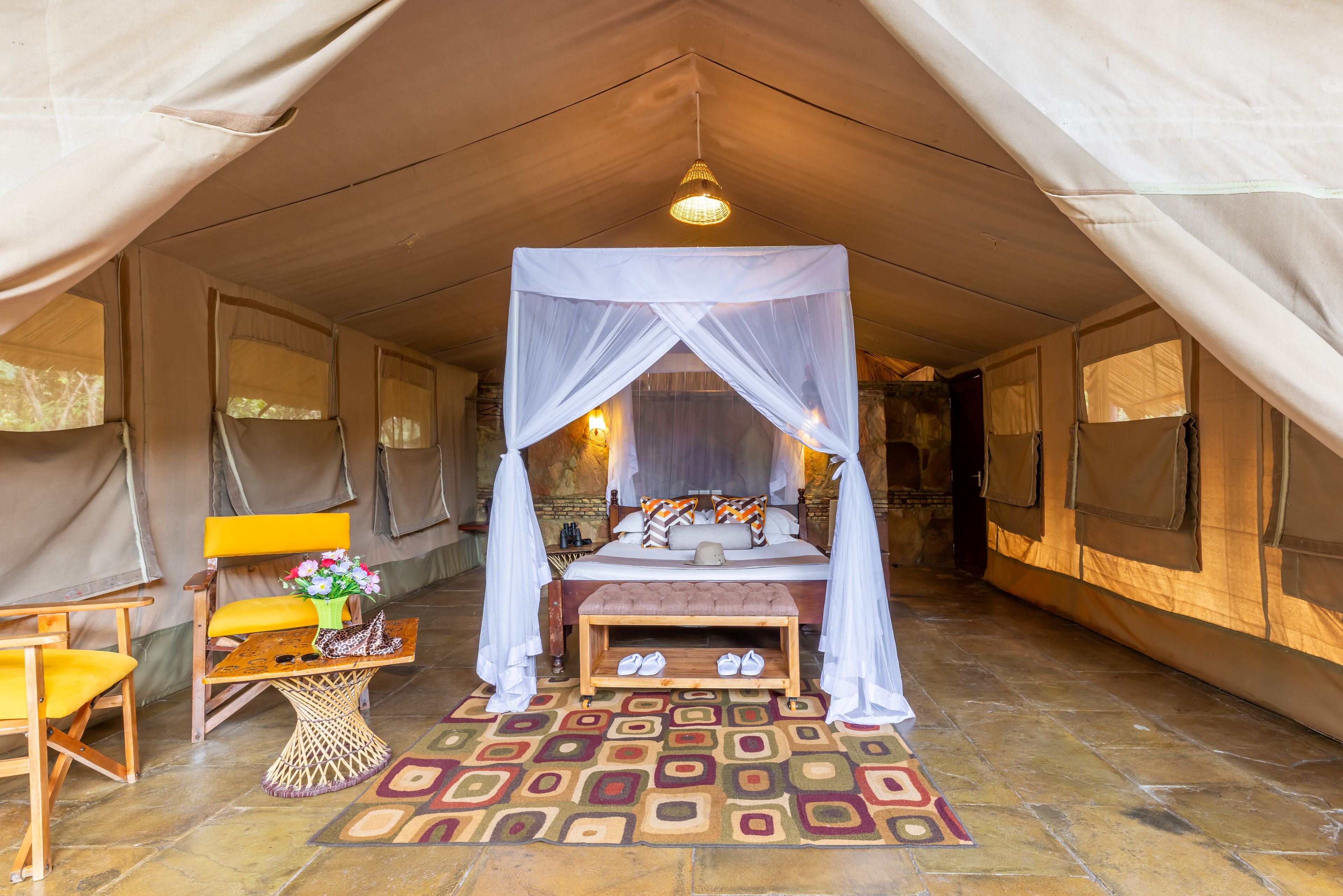 Een tent met een bed, een bank met schoenen, een stoel en een tafel met een bloevas.